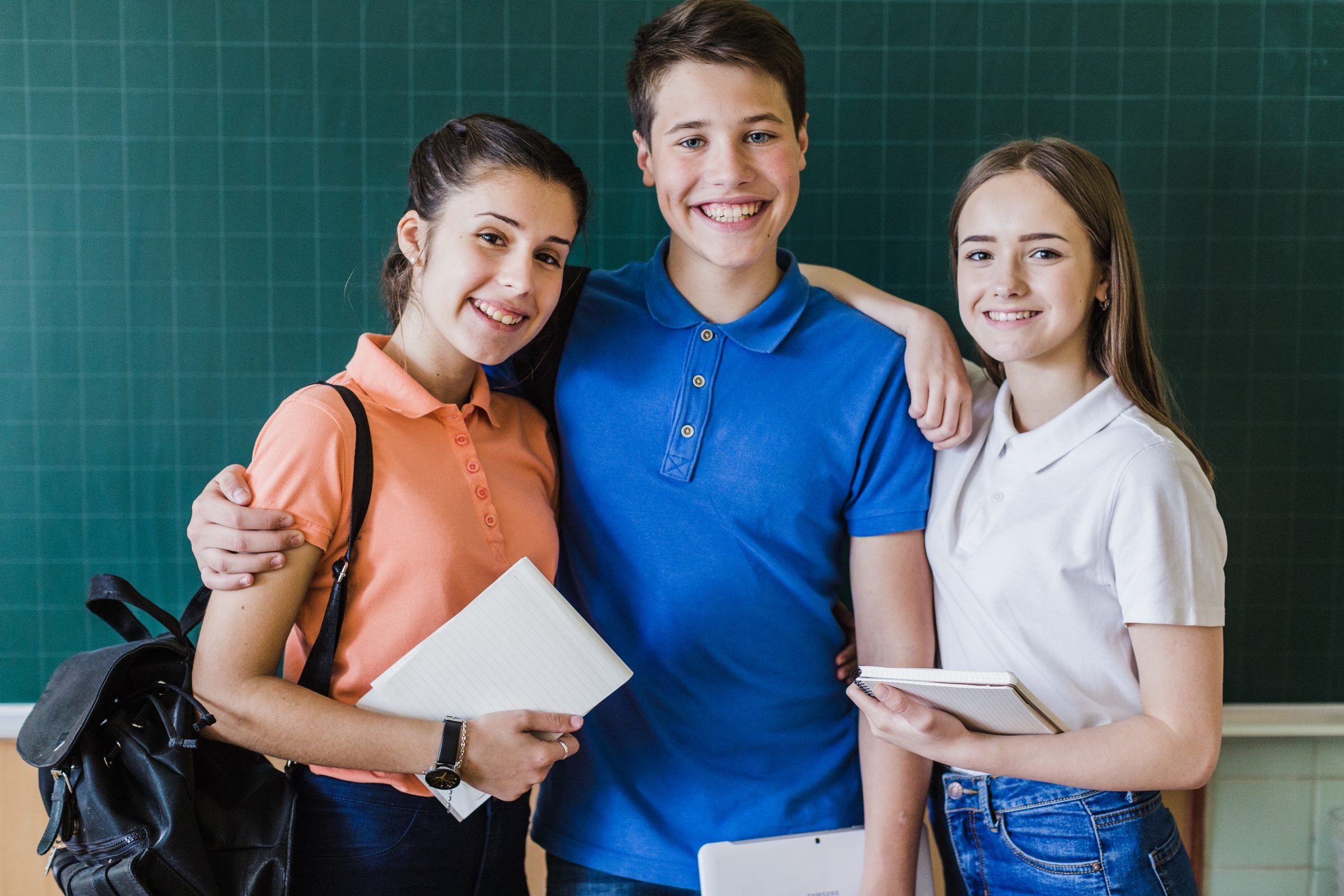 Tres estudiantes de enseñanza media sonriendo frente a una pizarra